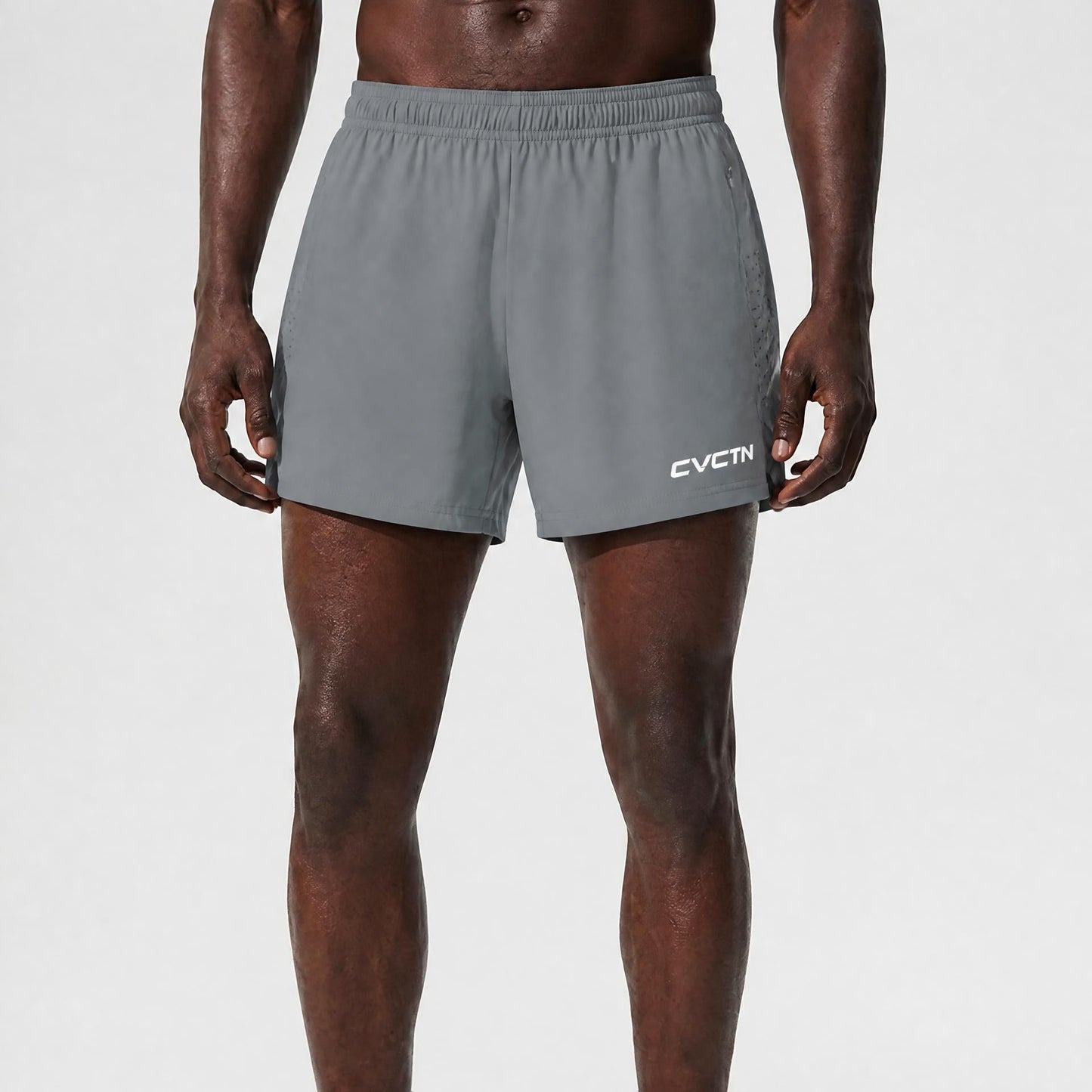A model wearing gray athletic shorts with a white CVCIN logo on the lower left leg, paired with white socks and white sneakers, shown from the waist down against a light gray studio background.